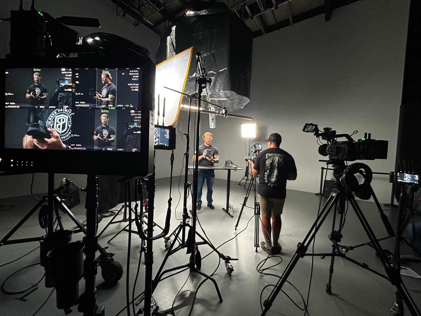 A studio interview setup seen from behind the monitors, subject lit at a table between two cameras